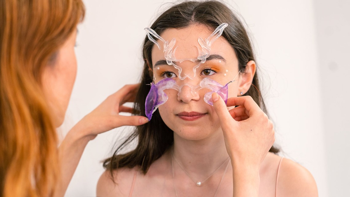 woman affixing decorative prostheses to a model's face