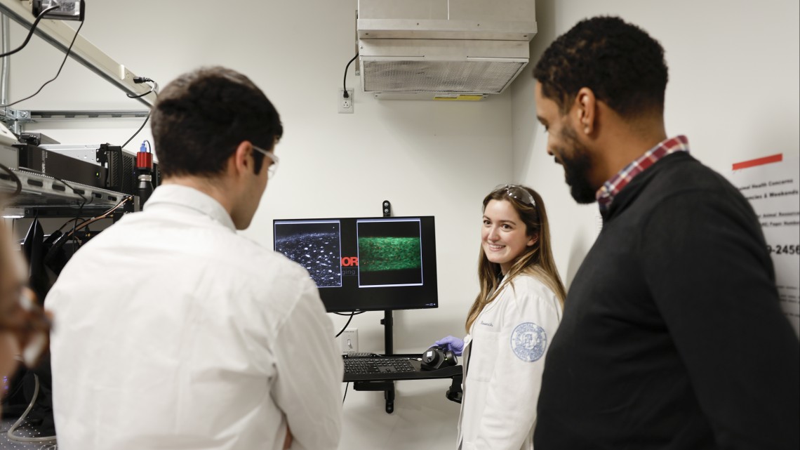 three scientists look at a computer monitor in a lab