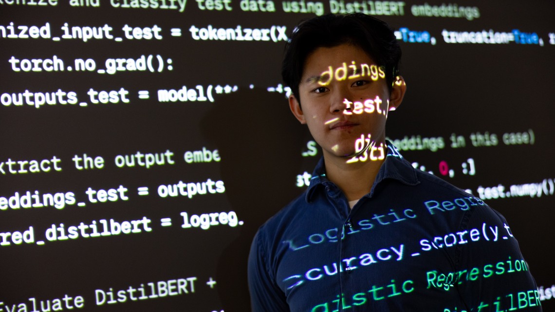 student in front of screen with text projecting over his face