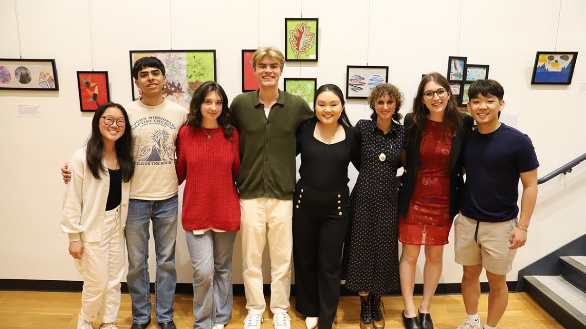 eight people smile at camera, standing in front of art on the wall