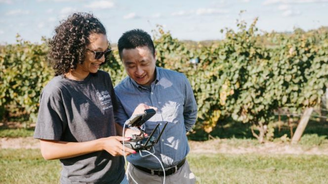 Professor and student operating a drone in an orchard