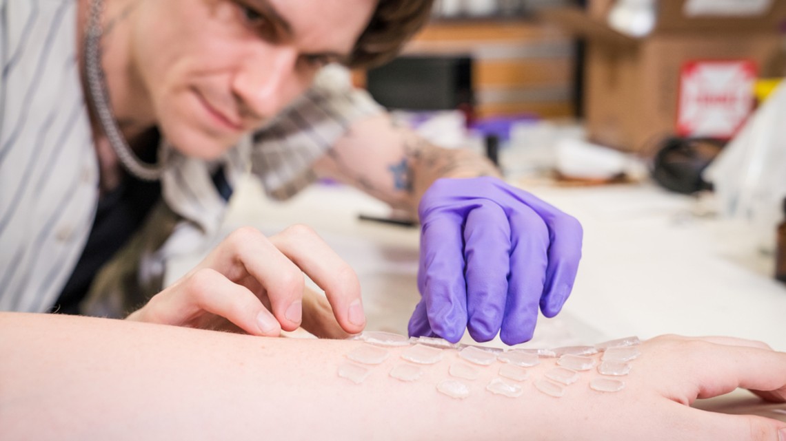 Artist Joe George applies 3-d printed resin scales to a person's arm.
