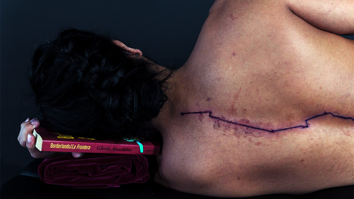 man laying on his side with back to the camera revealing a bleeding wound running down his spine