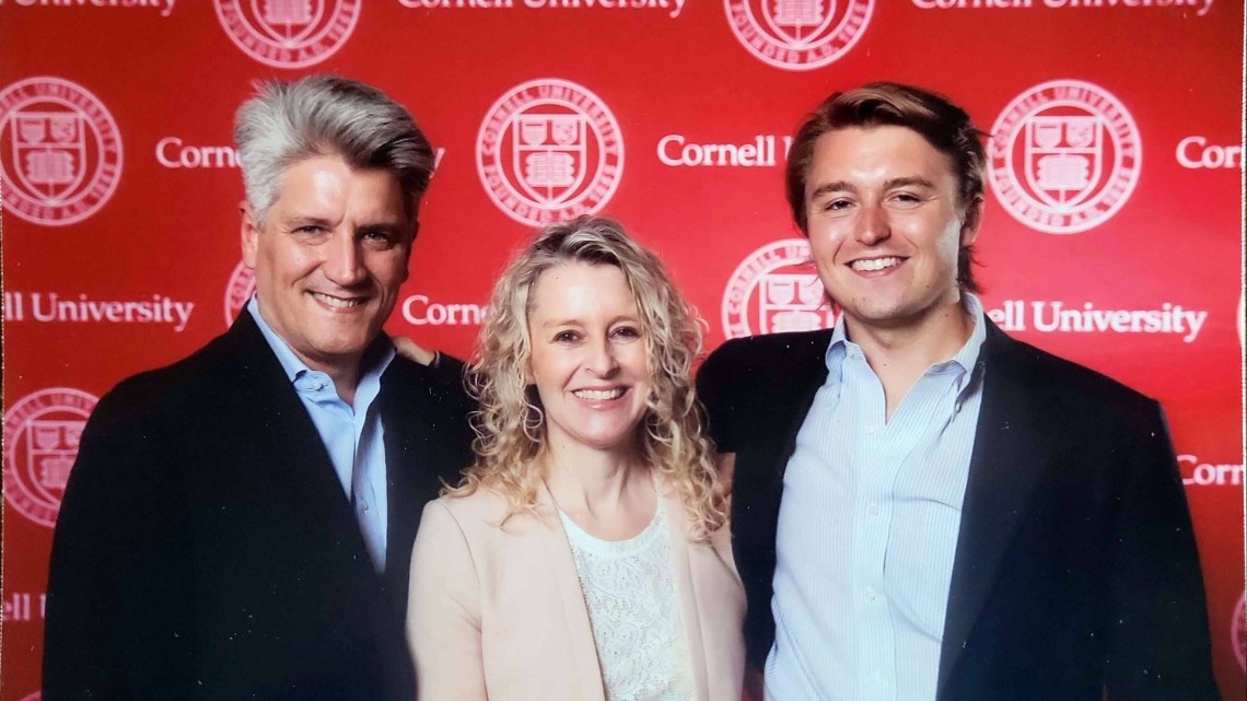 David, Laura and Ryan Nowicki stand together in front of a Cornell seal background