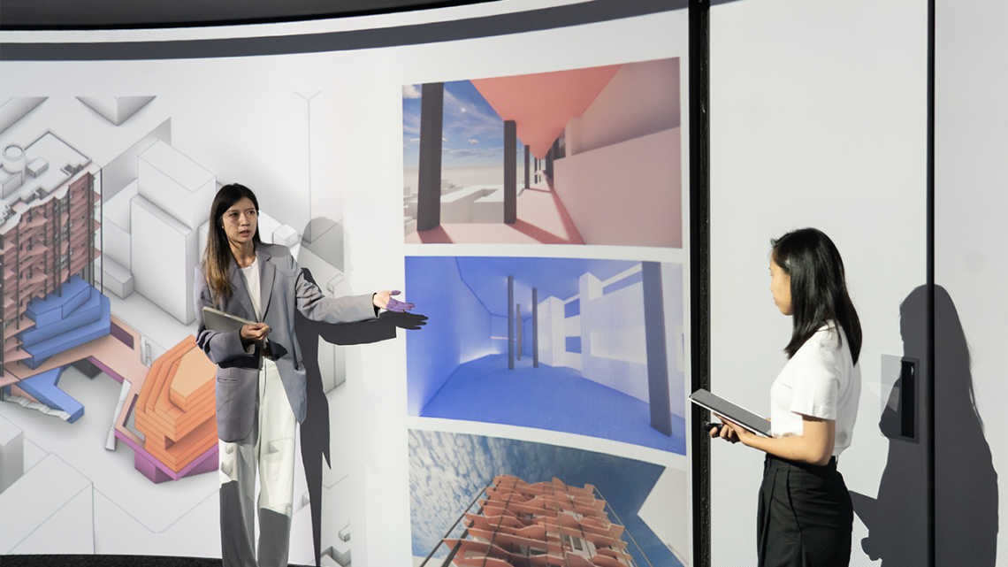 Two students presenting designs in front of a digital projection screen