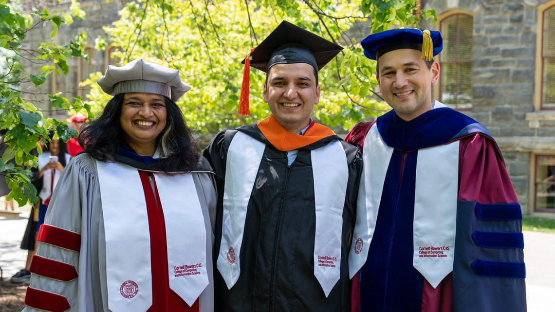 Three people - a dean, a student and professor - stand in graduation regalia.