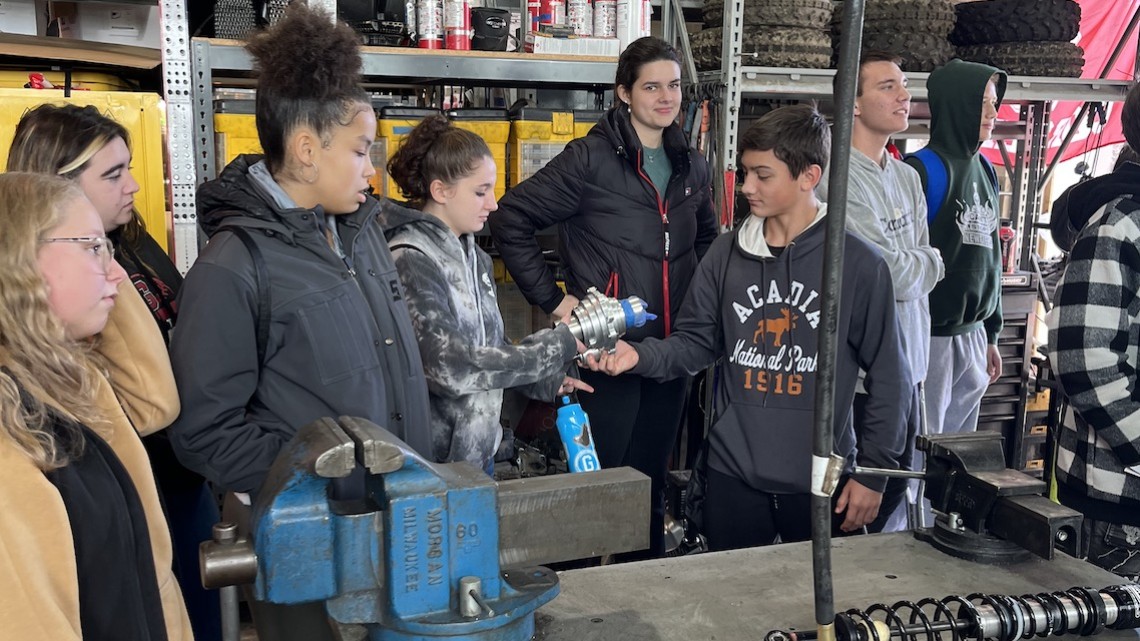 eight students examine mechanical gear