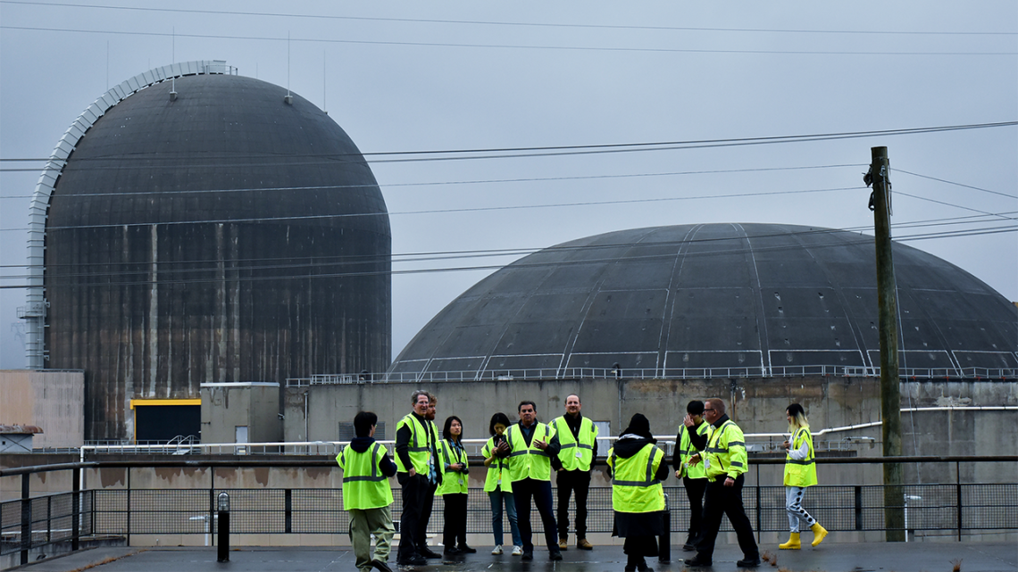 People wearing neon construction vests gathered outside a power plant on a stormy day