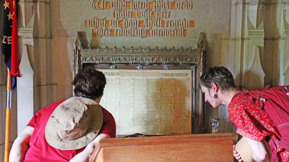 two people peering at list of names on vintage campus memorial