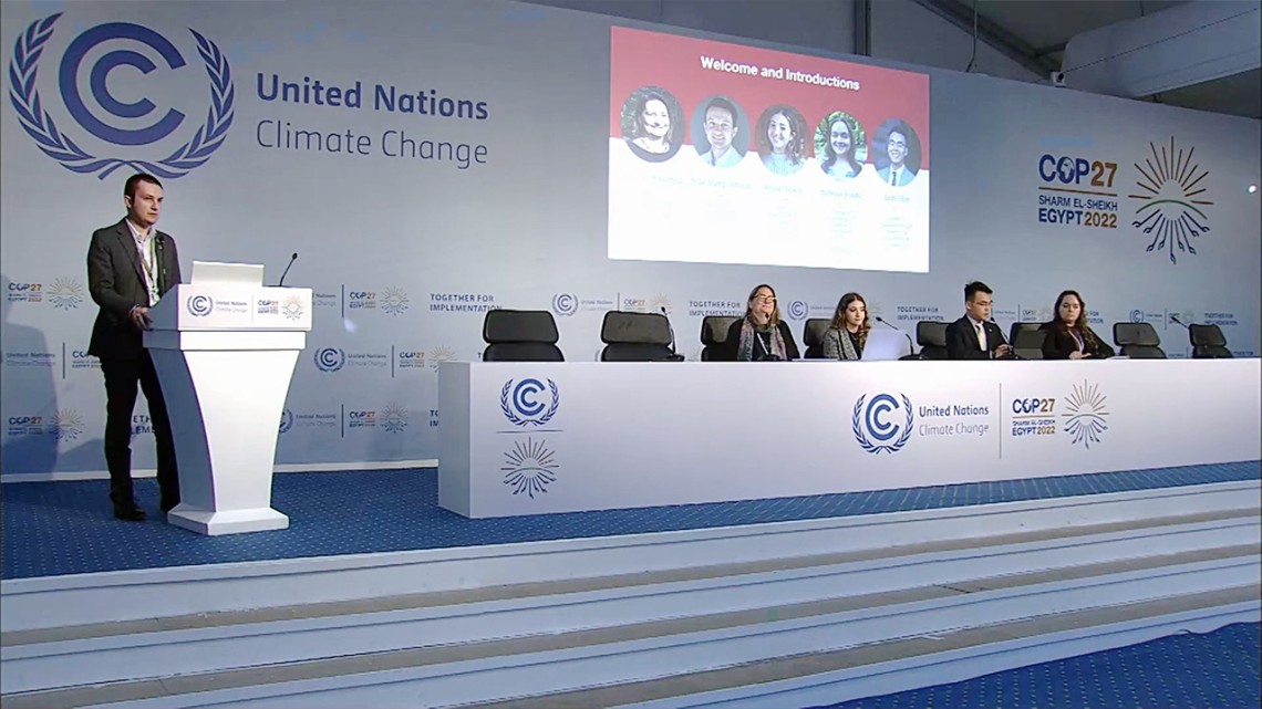 Nick Hamp-Adams stands at podium in a news conference setting at COP27