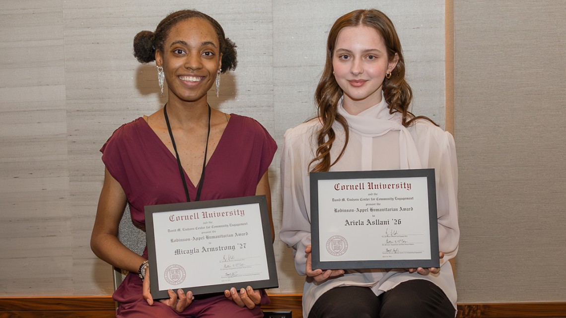 Two students smile at the camera holding award certificates