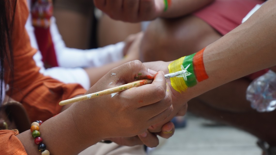 Hands paint the Myanmar flag on a wrist