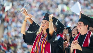 Graduates cheering while confetti falls. 