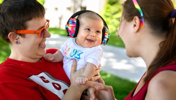 Two women with a smiling baby wearing noise-cancelling headphones. 