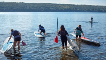 Paddleboarders head into Cayuga Lake at Merrill Family Sailing Center for a class with Cornell Outdoor Education.