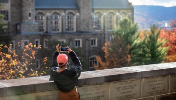 A student pauses to take a photo of the sunset from the Founders Wall outside Uris Library.