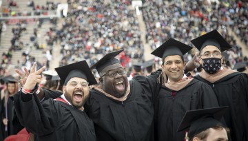 Four graduates cheer and laugh. 