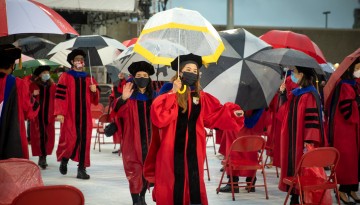 PhD candidates enter the field holding umbrellas. 