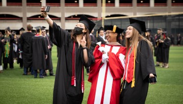 Two graduates pose with the University Marshall. 