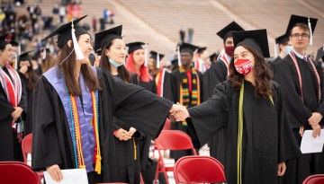 Two graduates hold hands across the aisle. 