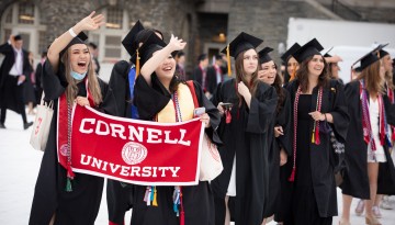 Graduates hold Cornell University banner and wave to the crowd. 