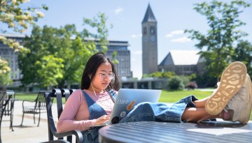 A recent CALS grad works on a laptop outside Goldwin Smith Hall.