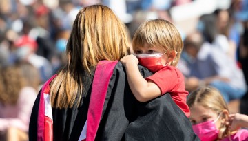 A graduate holds a small child. 