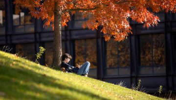 A student works on the sunny slope near Uris Hall. 