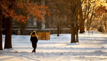 Student walks through a snowy Arts Quad at sunset.
