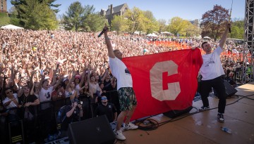 Two performers hold a Cornell "C" banner on the stage. 