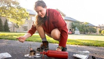 A Cornell Outdoor Education student tests a camp stove after a night of camping on the Arts Quad.