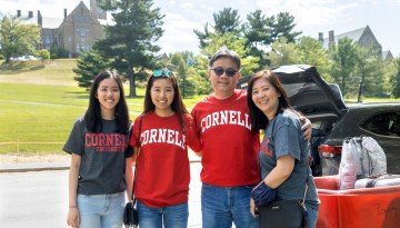 A family of four wearing Cornell t-shirts poses in front of a car and moving bin. 