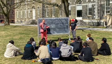 Students gather for class in front of Sibley Hall on a warm spring day.