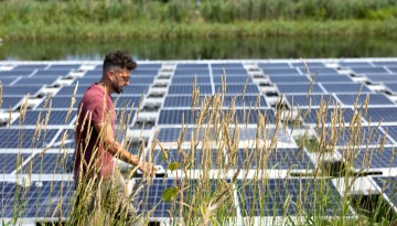 A man walks past solar panels installed in a pond. 
