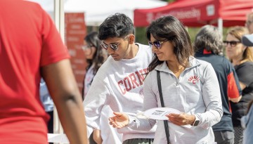 Two people in Cornell shirts browse at an information table. 
