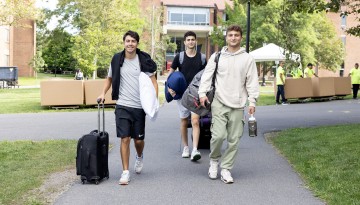 Three young men carrying belongings make their way to the dorms.
