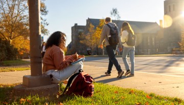 A student studies along College Avenue while waiting for a bus.