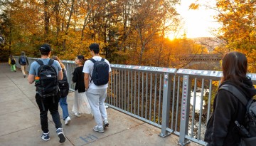Students cross the footbridge into Collegetown as the evening sun sets.