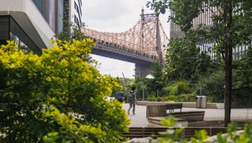 Individuals walking on Cornell Tech's campus with the Queensboro Bridge in view.
