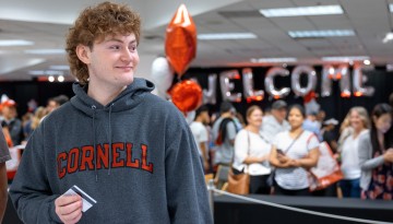 A student in a Cornell hoodie holds his new ID card. 