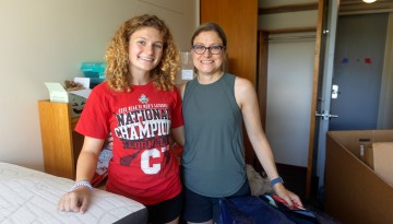 A mom and daughter pose in a dorm room. 