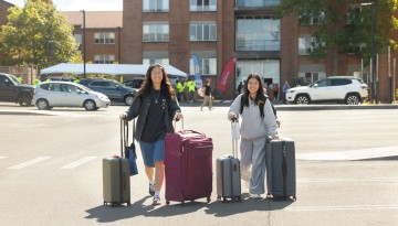 Students roll luggage across a parking lot. 