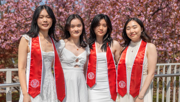 Four students wearing white pose for photos in front of pink flowering trees