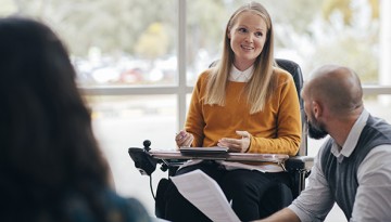 A young woman in a wheelchair speaks with co-workers